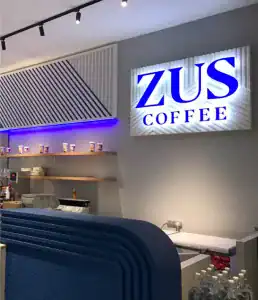 Modern coffee shop interior with ZUS Coffee sign illuminated, stylish decor, display shelves with coffee cups, and customer counter setup in Malaysia for franchise opportunities.